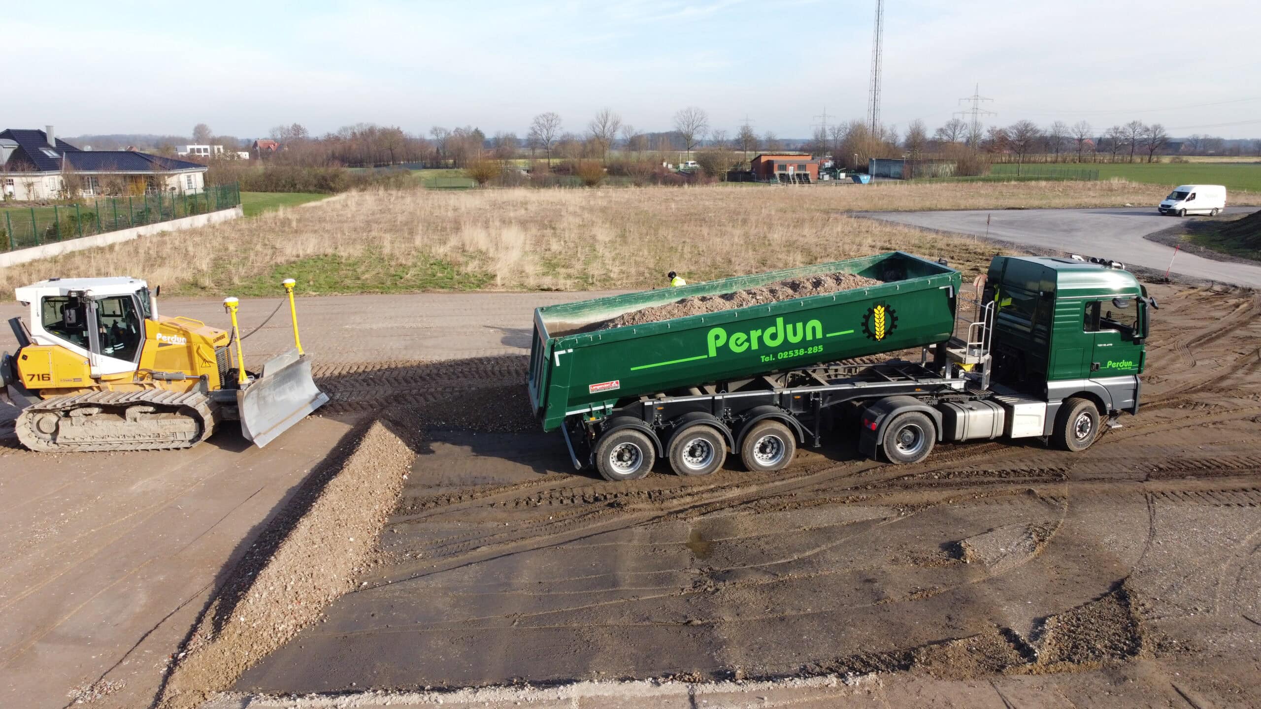 Lkw mit grünem Anhänger und Traktor schaufeln Kies auf Baustelle - Matschige Umgebung, braune Wiese.