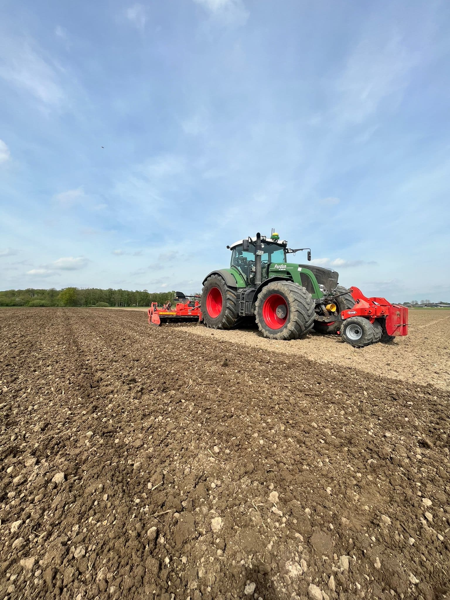 Ein grüner Traktor pflügt ein Feld unter blauem Himmel; rote Details und große schwarze Reifen.