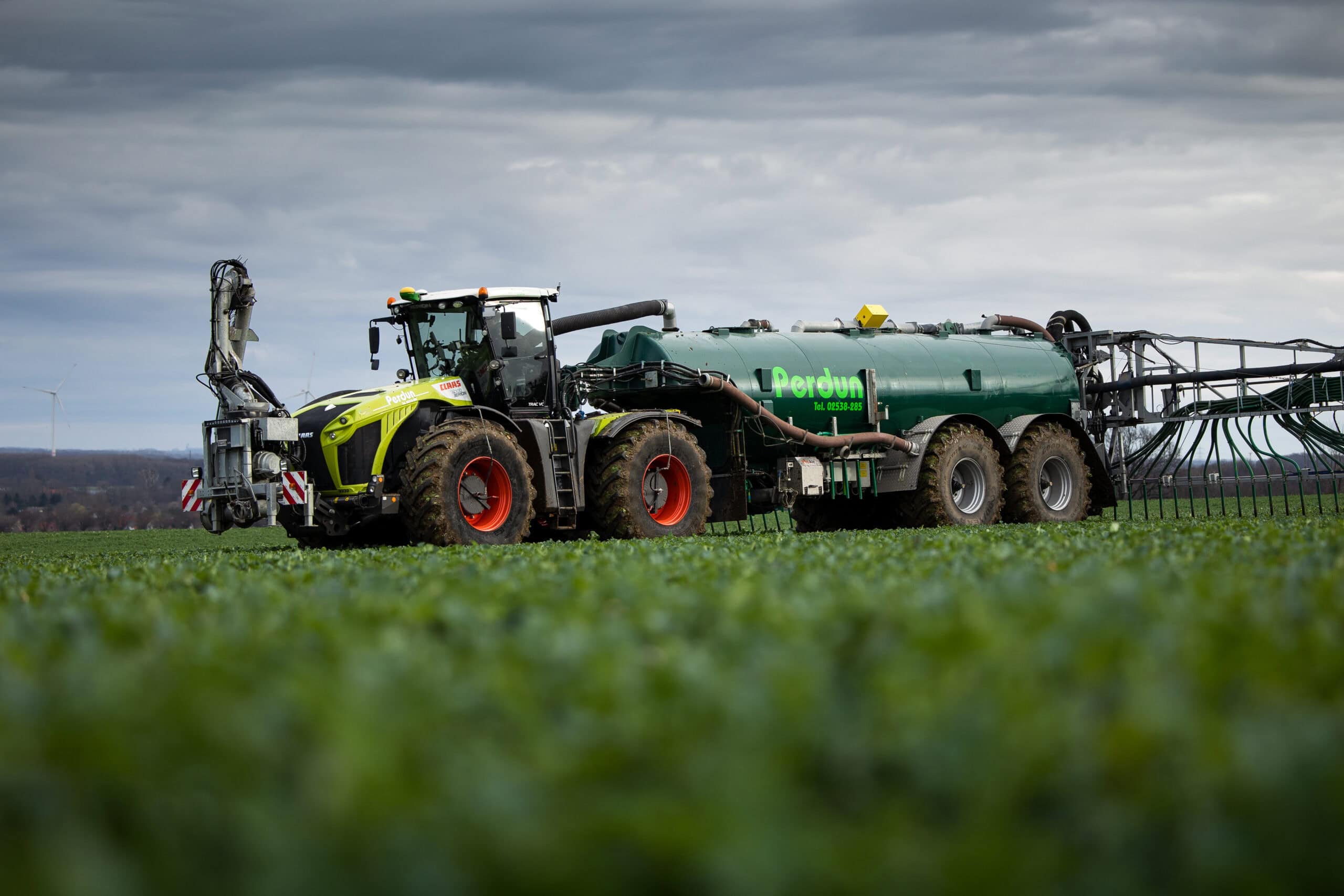 Ein Traktor zieht einen Anhänger über ein grünes Feld unter bewölktem Himmel. Traktor in Grün und Grau.